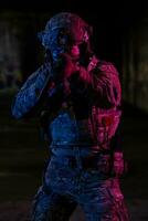 Army soldier in Combat Uniforms with an assault rifle and combat helmet night mission dark background. Blue and purple gel light effect. photo