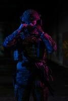 Ejército soldado en combate uniformes con un asalto rifle y combate casco noche misión oscuro antecedentes. azul y púrpura gel ligero efecto. foto