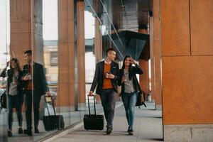 Business man and business woman talking and holding luggage traveling on a business trip, carrying fresh coffee in their hands.Business concept photo