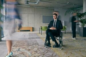 A businessman in a wheelchair in a modern office, surrounded by his colleagues who are portrayed with blurred movements, symbolizing their support and solidarity as they navigate the workspace together. photo