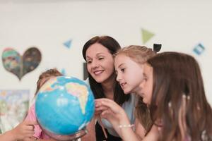 Female teacher with kids in geography class looking at globe. Side view of group of diverse happy school kids with globe in classroom at school. photo