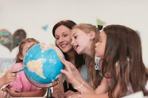 Female teacher with kids in geography class looking at globe. Side view of group of diverse happy school kids with globe in classroom at school. photo