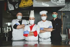 group chefs standing together in the kitchen at restaurant wearing protective medical mask and gloves in coronavirus new normal concept photo