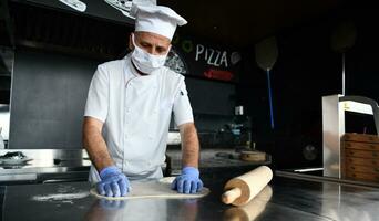 chef  with protective coronavirus face mask preparing pizza photo