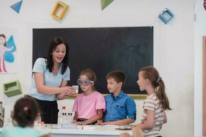 Elementary School Science Classroom Enthusiastic Teacher Explains Chemistry to Diverse Group of Children, Little Boy Mixes Chemicals in Beakers. Children Learn with Interest photo