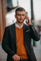 Going to airport terminal. Confident businessman traveler walking on city streets and pulling his suitcase drinking coffee and speaking on smartphone photo