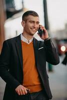 Going to airport terminal. Confident businessman traveler walking on city streets and pulling his suitcase drinking coffee and speaking on smartphone photo