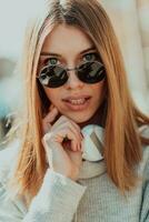 a modern girl with sunglasses walking down the street listens to music in headphones. photo