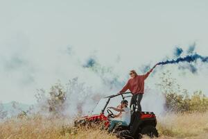 Group of young happy excited people having fun enjoying beautiful sunny day holding colorful torches while driving a off road buggy car on mountain nature. photo