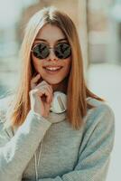 a modern girl with sunglasses walking down the street listens to music in headphones. photo