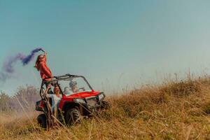 Group of young happy excited people having fun enjoying beautiful sunny day holding colorful torches while driving a off road buggy car on mountain nature. photo