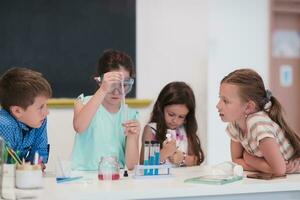 Elementary School Science Classroom Enthusiastic Teacher Explains Chemistry to Diverse Group of Children, Little Boy Mixes Chemicals in Beakers. Children Learn with Interest photo