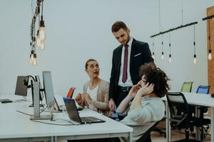 grupo de multiétnico colegas trabajando en escritorio ordenadores, ordenador portátil y compartiendo su ideas en un moderno oficina espacio.joven influencers trabajo en en línea márketing proyectos foto