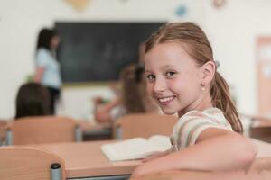 Little girls sitting in elementary school drawing on paper with their friends while sitting in a modern classroom photo