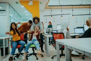 Team building and office fun. Young cheerful businesspeople in smart casual wear having fun while racing on office chairs and smiling. photo