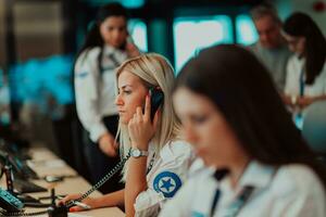 hembra seguridad Guardia operador hablando en el teléfono mientras trabajando a puesto de trabajo con múltiple muestra seguridad guardias trabajando en múltiple monitores foto