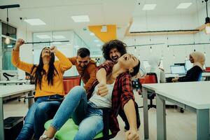 Team building and office fun. Young cheerful businesspeople in smart casual wear having fun while racing on office chairs and smiling. photo