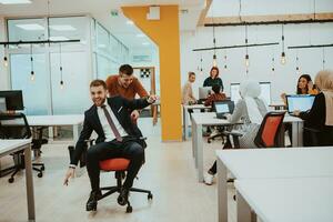 Team building and office fun. Young cheerful businesspeople in smart casual wear having fun while racing on office chairs and smiling. photo