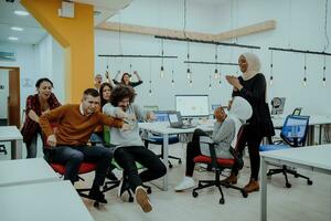 Team building and office fun. Young cheerful businesspeople in smart casual wear having fun while racing on office chairs and smiling. photo