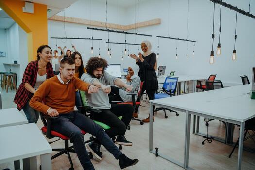 Team building and office fun. Young cheerful businesspeople in smart casual wear having fun while racing on office chairs and smiling. photo