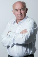 Confident senior man in white shirt crossing hands on chest and looking at camera while standing against gray background. Self confident senior isolated white studio shoot. photo