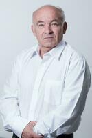 Portrait of an older man wearing a white shirt on a gray background. A healthy old man looks at a camera isolated over a gray wall. An older man smiles at the camera, a happy old man. photo