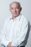 Portrait of an older man wearing a white shirt on a gray background. A healthy old man looks at a camera isolated over a gray wall. An older man smiles at the camera, a happy old man. photo