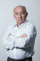 Confident senior man in white shirt crossing hands on chest and looking at camera while standing against gray background. Self confident senior isolated white studio shoot. photo