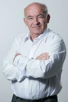 Confident senior man in white shirt crossing hands on chest and looking at camera while standing against gray background. Self confident senior isolated white studio shoot. photo