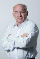 Confident senior man in white shirt crossing hands on chest and looking at camera while standing against gray background. Self confident senior isolated white studio shoot. photo