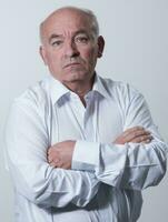 Confident senior man in white shirt crossing hands on chest and looking at camera while standing against gray background. Self confident senior isolated white studio shoot. photo