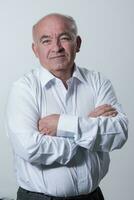 Confident senior man in white shirt crossing hands on chest and looking at camera while standing against gray background. Self confident senior isolated white studio shoot. photo