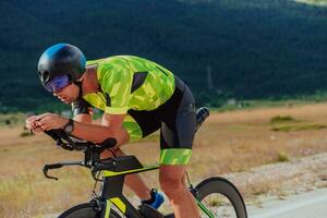 cerca arriba foto de un activo triatleta en ropa de deporte y con un protector casco montando un bicicleta. selectivo atención