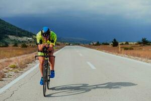 lleno longitud retrato de un activo triatleta en ropa de deporte y con un protector casco montando un bicicleta. selectivo atención foto