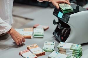 Bank employees using money counting machine while sorting and counting paper banknotes inside bank vault. Large amounts of money in the bank photo