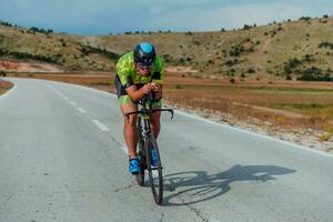 lleno longitud retrato de un activo triatleta en ropa de deporte y con un protector casco montando un bicicleta. selectivo atención foto