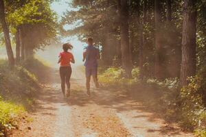 Pareja disfrutando en un sano estilo de vida mientras trotar en un país la carretera mediante el hermosa soleado bosque, ejercicio y aptitud concepto foto