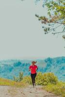 joven contento mujer disfrutando en un sano estilo de vida mientras trotar en un país la carretera mediante el hermosa soleado bosque, ejercicio y aptitud concepto foto