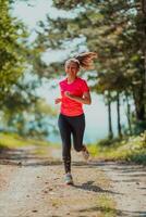 joven contento mujer disfrutando en un sano estilo de vida mientras trotar en un país la carretera mediante el hermosa soleado bosque, ejercicio y aptitud concepto foto