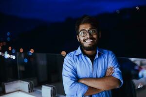 An Indian man with glasses and a blue shirt looks around the city at night. In the background of the night street of the city photo