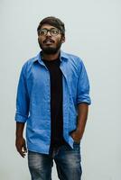 indio sonriente joven hombre con azul camisa y lentes posando en gris antecedentes foto