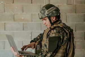 American soldier in military uniform using laptop computer for drone controlling and to stay in contact with friends and family photo