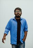 Indian smiling young man with blue shirt and glasses posing on gray background photo