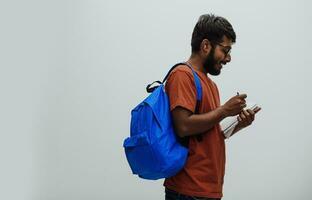 Indian student with blue backpack, glasses and notebook posing on gray background. The concept of education and schooling. Time to go back to school photo