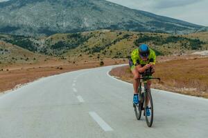 Full length portrait of an active triathlete in sportswear and with a protective helmet riding a bicycle. Selective focus photo