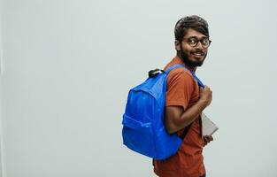 Indian student with blue backpack, glasses and notebook posing on gray background. The concept of education and schooling. Time to go back to school photo