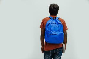 Indian student with blue backpack, glasses and notebook posing on gray background. The concept of education and schooling. Time to go back to school photo