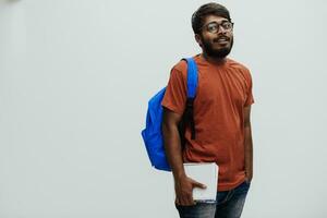 Indian student with blue backpack, glasses and notebook posing on gray background. The concept of education and schooling. Time to go back to school photo