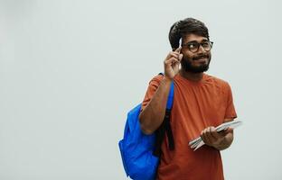 Confused indian student with blue backpack, glasses and notebook posing on gray background. The concept of education and schooling. Time to go back to school photo