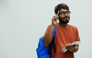 Confused indian student with blue backpack, glasses and notebook posing on gray background. The concept of education and schooling. Time to go back to school photo